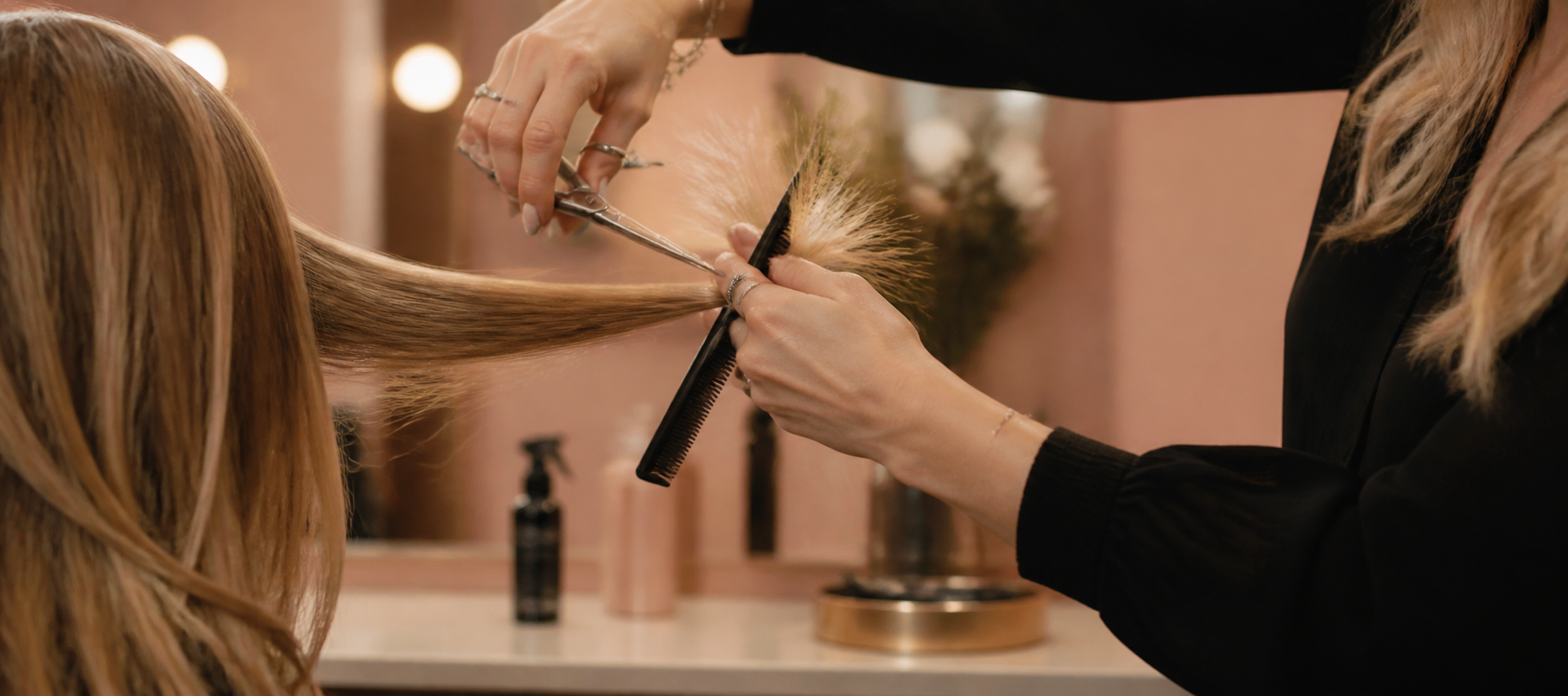 A stylist cutting hair with scissors and a comb in a warm, softly lit salon interior